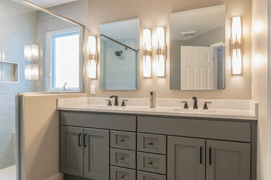 Example of a mid-sized transitional master gray tile and ceramic tile ceramic tile, beige floor and double-sink corner shower design in Detroit with recessed-panel cabinets, gray cabinets, a two-piece toilet, beige walls, an undermount sink, quartz countertops, a hinged shower door, white countertops, a niche and a built-in vanity