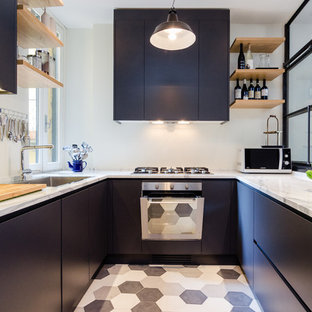 Modelo de cocina en U, industrial, de tamaño medio, sin isla, con fregadero de un seno, armarios con paneles lisos, electrodomésticos de acero inoxidable, puertas de armario negras, encimera de mármol y suelo de baldosas de cerámica