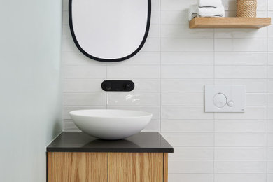 Small modern shower room bathroom in Toronto with flat-panel cabinets, medium wood cabinets, a walk-in shower, a wall mounted toilet, white tiles, ceramic tiles, green walls, concrete flooring, a vessel sink, engineered stone worktops, multi-coloured floors, an open shower, black worktops, a single sink and a floating vanity unit.