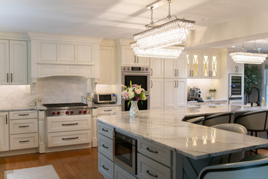 Eat-in kitchen - large traditional l-shaped medium tone wood floor and brown floor eat-in kitchen idea in New York with a farmhouse sink, recessed-panel cabinets, white cabinets, quartz countertops, gray backsplash, stone tile backsplash, paneled appliances, an island and gray countertops