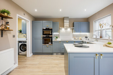 Photo of a medium sized contemporary u-shaped kitchen/diner in Dorset with a built-in sink, shaker cabinets, blue cabinets, white splashback, medium hardwood flooring, no island, beige floors and white worktops.