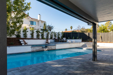 Imagen de piscina alargada minimalista grande rectangular en patio trasero con paisajismo de piscina y adoquines de hormigón