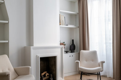 パリにある高級な中くらいなおしゃれなLDK (ライブラリー、白い壁、淡色無垢フローリング、標準型暖炉、漆喰の暖炉まわり、テレビなし、ベージュの床) の写真