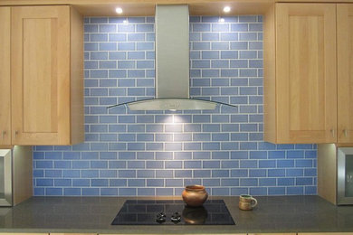 Kitchen - mid-sized transitional kitchen idea in Phoenix with a farmhouse sink, shaker cabinets, light wood cabinets, recycled glass countertops, blue backsplash, subway tile backsplash and black appliances