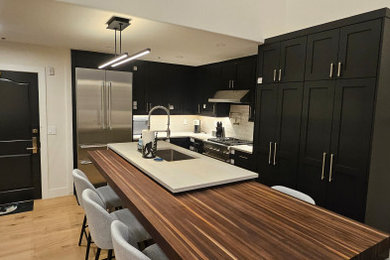 Example of a mid-sized transitional l-shaped brown floor and vaulted ceiling eat-in kitchen design in Denver with an undermount sink, black cabinets, quartz countertops, white backsplash, porcelain backsplash, stainless steel appliances, an island and gray countertops
