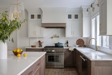 Photo of a large traditional u-shaped kitchen/diner in Boston with a single-bowl sink, shaker cabinets, medium wood cabinets, engineered stone countertops, white splashback, engineered quartz splashback, stainless steel appliances, light hardwood flooring, an island, brown floors and white worktops.