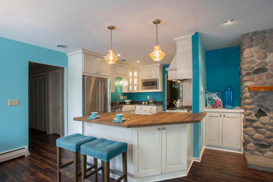Mid-sized beach style u-shaped vinyl floor and brown floor open concept kitchen photo in Milwaukee with a farmhouse sink, white cabinets, wood countertops, stainless steel appliances, recessed-panel cabinets, white backsplash, ceramic backsplash and a peninsula