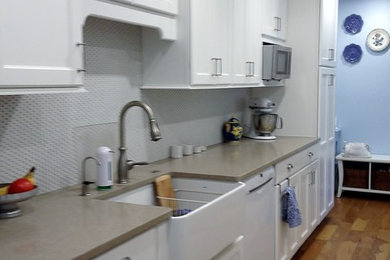 Example of a transitional galley medium tone wood floor kitchen design in Austin with recessed-panel cabinets, white cabinets, quartz countertops, a farmhouse sink, white backsplash, ceramic backsplash and white appliances