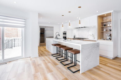 Photo of a large contemporary l-shaped eat-in kitchen in Toronto with an undermount sink, flat-panel cabinets, white cabinets, quartz benchtops, white splashback, engineered quartz splashback, stainless steel appliances, porcelain floors, with island and white benchtop.
