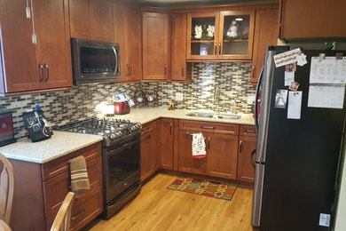 Photo of a small transitional l-shaped eat-in kitchen in Milwaukee with an undermount sink, shaker cabinets, medium wood cabinets, quartz benchtops, beige splashback, glass tile splashback, stainless steel appliances, laminate floors and no island.