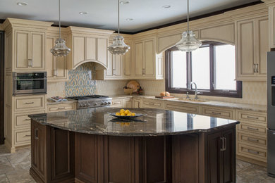 Kitchen pantry - large transitional l-shaped travertine floor and multicolored floor kitchen pantry idea in Kansas City with an undermount sink, recessed-panel cabinets, beige cabinets, granite countertops, beige backsplash, ceramic backsplash, stainless steel appliances and an island