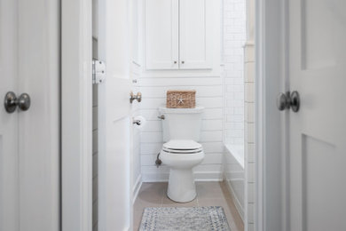 Photo of a small beach style master bathroom in New York with shaker cabinets, white cabinets, engineered quartz benchtops, a single vanity, a built-in vanity, an alcove tub, a shower/bathtub combo, a two-piece toilet, gray tile, stone tile, ceramic floors, an undermount sink, a shower curtain, white benchtops, a niche and planked wall panelling.