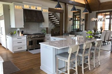 This is an example of an expansive country u-shaped eat-in kitchen in Philadelphia with an undermount sink, shaker cabinets, white cabinets, quartzite benchtops, beige splashback, ceramic splashback, stainless steel appliances, medium hardwood floors, with island and brown floor.