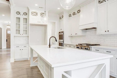 Photo of a mid-sized country l-shaped eat-in kitchen in Miami with an undermount sink, shaker cabinets, white cabinets, quartz benchtops, white splashback, subway tile splashback, stainless steel appliances, light hardwood floors, with island, brown floor and white benchtop.