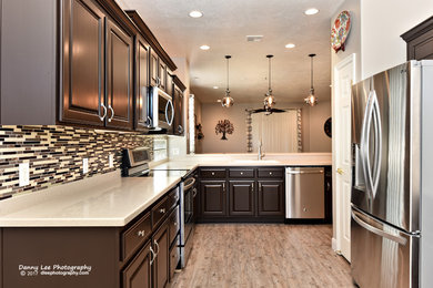 Open concept kitchen - mid-sized contemporary l-shaped vinyl floor open concept kitchen idea in Salt Lake City with a double-bowl sink, raised-panel cabinets, brown cabinets, solid surface countertops, multicolored backsplash, ceramic backsplash, stainless steel appliances and a peninsula