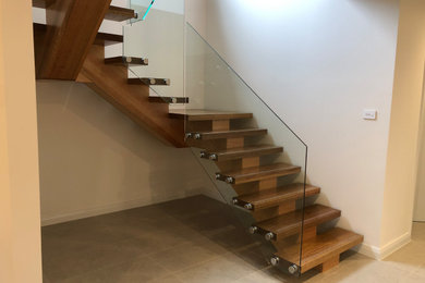 Mid-sized modern wood u-shaped staircase in Sydney with glass railing.