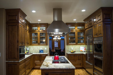 Photo of a mid-sized traditional u-shaped eat-in kitchen in Denver with an undermount sink, raised-panel cabinets, dark wood cabinets, granite benchtops, multi-coloured splashback, glass tile splashback, stainless steel appliances, light hardwood floors and with island.