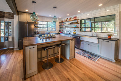 Large transitional l-shaped medium tone wood floor open concept kitchen photo in Other with a farmhouse sink, open cabinets, medium tone wood cabinets, concrete countertops, white backsplash, subway tile backsplash, black appliances and an island