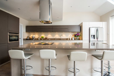 Contemporary single-wall open plan kitchen in London with a double-bowl sink, flat-panel cabinets, beige cabinets, quartzite benchtops and stainless steel appliances.