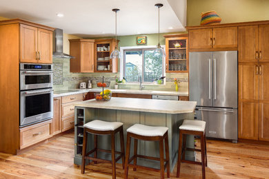 Inspiration for a mid-sized timeless medium tone wood floor eat-in kitchen remodel in San Francisco with an undermount sink, shaker cabinets, green cabinets, solid surface countertops, green backsplash, glass tile backsplash, stainless steel appliances and an island
