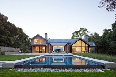 Modelo de piscina infinita campestre grande rectangular en patio trasero con paisajismo de piscina y adoquines de piedra natural