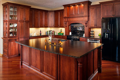 Example of a large classic l-shaped dark wood floor kitchen design in Omaha with an undermount sink, raised-panel cabinets, dark wood cabinets, granite countertops, black backsplash, cement tile backsplash, black appliances and an island