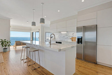 Photo of a mid-sized contemporary galley eat-in kitchen in Melbourne with a single-bowl sink, louvered cabinets, white cabinets, marble benchtops, grey splashback, marble splashback, stainless steel appliances, medium hardwood floors, with island, brown floor and grey benchtop.