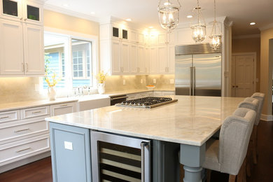 This is an example of a large traditional l-shaped eat-in kitchen in New York with a farmhouse sink, beige splashback, stone slab splashback, stainless steel appliances, dark hardwood floors, with island, white cabinets, recessed-panel cabinets and granite benchtops.
