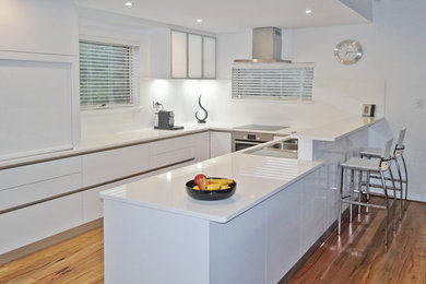 Design ideas for a large modern u-shaped open plan kitchen in Perth with a double-bowl sink, flat-panel cabinets, white cabinets, quartz benchtops, white splashback, glass sheet splashback, stainless steel appliances, medium hardwood floors, a peninsula and brown floor.