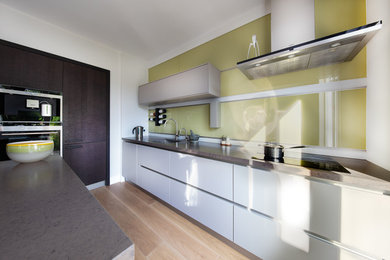 Inspiration for a mid-sized contemporary l-shaped eat-in kitchen in Oxfordshire with a single-bowl sink, flat-panel cabinets, grey cabinets, quartz benchtops, green splashback, glass sheet splashback, stainless steel appliances, light hardwood floors, with island, brown floor and brown benchtop.