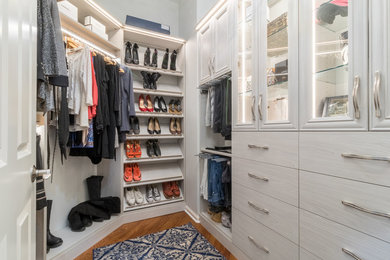 Photo of a mid-sized transitional women's walk-in wardrobe in Minneapolis with glass-front cabinets, light wood cabinets and medium hardwood floors.