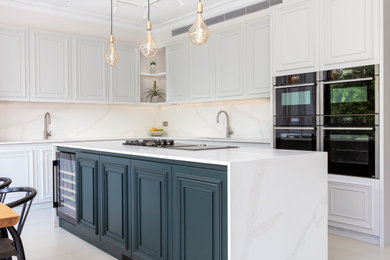 This is an example of a large contemporary l-shaped open plan kitchen in London with a built-in sink, beaded cabinets, green cabinets, engineered stone countertops, white splashback, engineered quartz splashback, black appliances, porcelain flooring, an island, beige floors, white worktops and feature lighting.