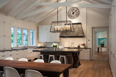 Eat-in kitchen - large farmhouse medium tone wood floor and brown floor eat-in kitchen idea in San Francisco with a farmhouse sink, shaker cabinets, white cabinets, white backsplash, subway tile backsplash, stainless steel appliances and an island
