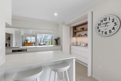 This is an example of a large modern galley kitchen pantry in Sunshine Coast with an undermount sink, white cabinets, quartz benchtops, black splashback, mirror splashback, stainless steel appliances, porcelain floors, with island, beige floor and white benchtop.