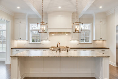 Example of a transitional medium tone wood floor and brown floor open concept kitchen design in Detroit with a farmhouse sink, shaker cabinets, white cabinets, marble countertops, white backsplash, stainless steel appliances, an island and brown countertops