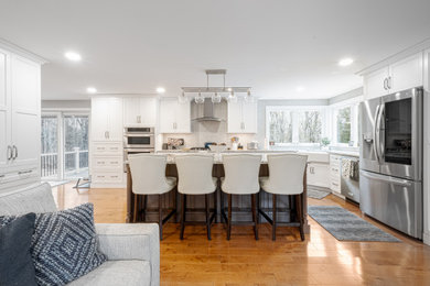 Eat-in kitchen - large transitional medium tone wood floor eat-in kitchen idea in Boston with a farmhouse sink, recessed-panel cabinets, white cabinets, granite countertops, gray backsplash, ceramic backsplash, stainless steel appliances, an island and gray countertops