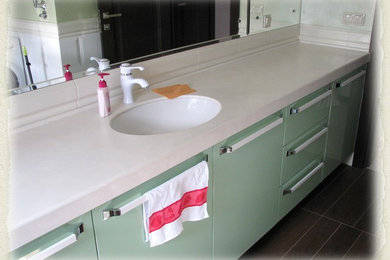 На фото: ванная комната среднего размера в современном стиле с плоскими фасадами, зелеными фасадами, белой плиткой, керамической плиткой, врезной раковиной, столешницей из искусственного камня и белой столешницей с