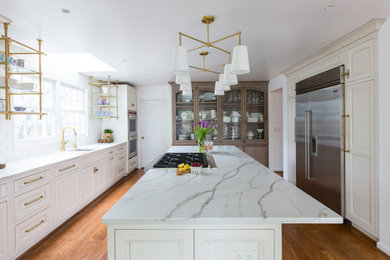 Photo of a large transitional u-shaped eat-in kitchen in Cincinnati with an undermount sink, recessed-panel cabinets, white cabinets, quartzite benchtops, white splashback, ceramic splashback, stainless steel appliances, medium hardwood floors, with island, brown floor and white benchtop.