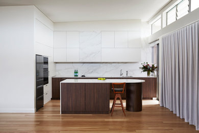 Foto på ett mellanstort funkis vit kök, med en integrerad diskho, släta luckor, skåp i mellenmörkt trä, bänkskiva i kvarts, flerfärgad stänkskydd, stänkskydd i porslinskakel, svarta vitvaror, ljust trägolv och en köksö