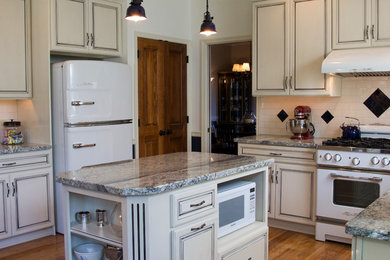 Example of a mid-sized farmhouse u-shaped medium tone wood floor open concept kitchen design in Philadelphia with a farmhouse sink, raised-panel cabinets, distressed cabinets, granite countertops, beige backsplash, subway tile backsplash, white appliances and an island