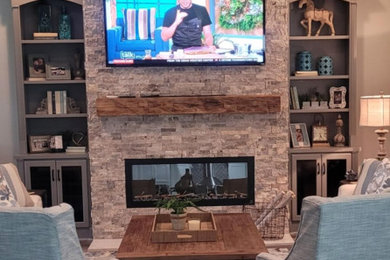 アトランタにある高級な中くらいなカントリー風のおしゃれなLDK (グレーの壁、無垢フローリング、標準型暖炉、石材の暖炉まわり、壁掛け型テレビ、茶色い床、格子天井) の写真