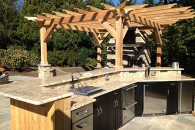 Large elegant backyard stone patio kitchen photo in New York with a pergola