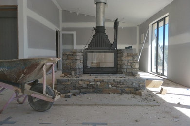 Cette photo montre une grande salle de séjour moderne ouverte avec une cheminée double-face et un manteau de cheminée en pierre.