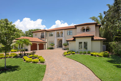 Large tuscan beige two-story stucco house exterior photo in Tampa with a hip roof and a tile roof