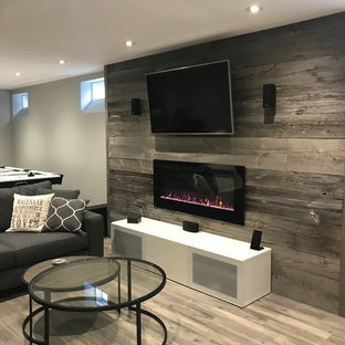 Diseño de sótano en el subsuelo contemporáneo, de tamaño medio, con paredes grises, suelo laminado, chimenea tradicional, marco de chimenea de madera y suelo gris