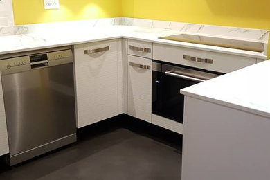 Cette image montre une cuisine ouverte minimaliste en U de taille moyenne avec une crédence jaune, un électroménager en acier inoxydable, un sol gris et un plan de travail blanc.