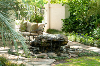 Ejemplo de patio tropical sin cubierta en patio con fuente y adoquines de piedra natural