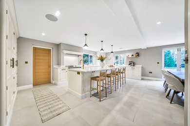 This is an example of an expansive beach style u-shaped open plan kitchen in Other with a belfast sink, beaded cabinets, white cabinets, quartz worktops, white splashback, stainless steel appliances, ceramic flooring, an island, beige floors and white worktops.