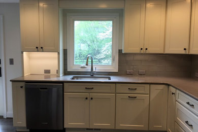 Photo of a mid-sized transitional l-shaped eat-in kitchen in Baltimore with an undermount sink, shaker cabinets, white cabinets, quartz benchtops, grey splashback, glass tile splashback, stainless steel appliances, medium hardwood floors, no island, grey floor and grey benchtop.