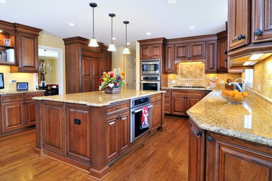 Inspiration for a mid-sized timeless l-shaped medium tone wood floor eat-in kitchen remodel in Chicago with a double-bowl sink, raised-panel cabinets, dark wood cabinets, granite countertops, beige backsplash, stone tile backsplash, paneled appliances and an island